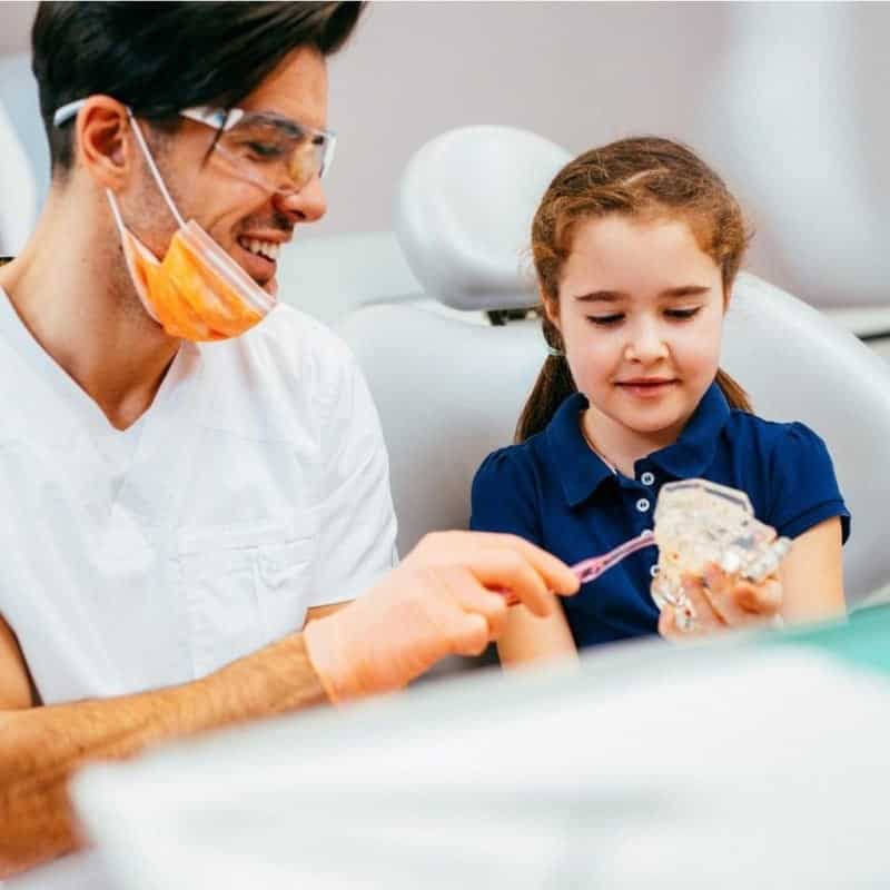 Young girl being shown how to brush her teeth by dentist