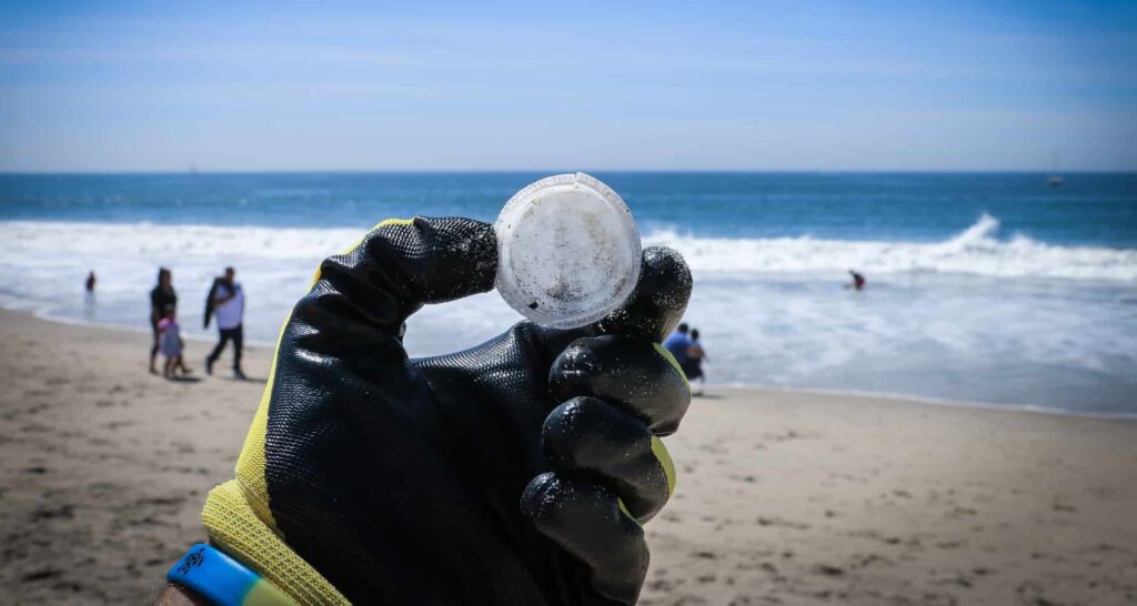 hand with single use plastic lid and sea behind